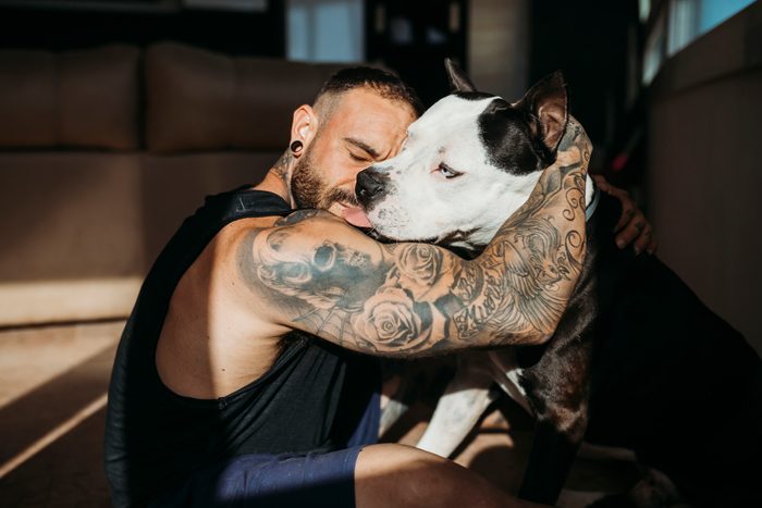 man with tattooed arm embracing dog at home