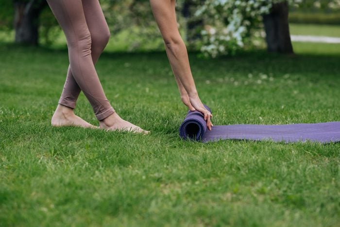 unrecognizable woman unrolls yoga mat in the park on the grass close-up