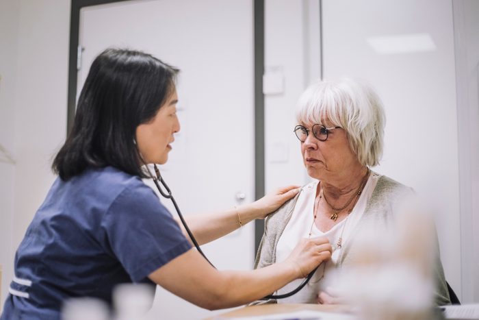 Female healthcare worker examining senior patient with stethoscope in medical clinic