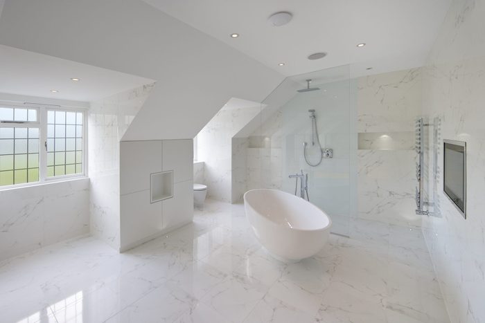 a large luxury white marble lined bathroom in an expensive home with a large oval bath