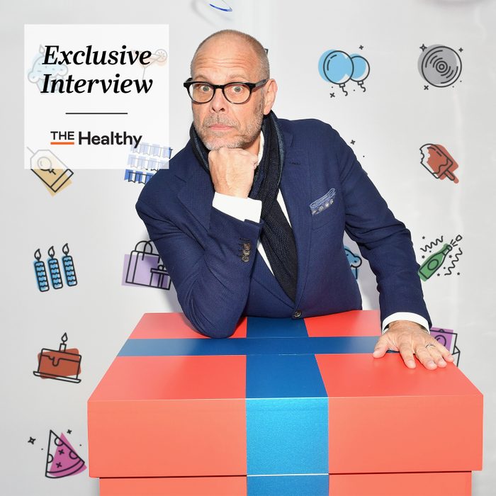 portrait of Alton Brown posing with a giant present with The Healthy Exclusive interview logo in the upper left corner
