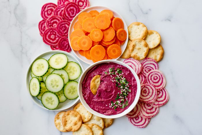 Bowl of beet hummus, vegetables and crackers on white marble counter.