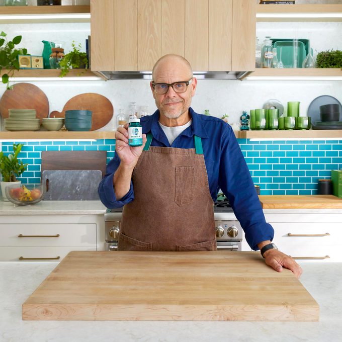 Alton Brown in a kitchen holding a bottle of capsules