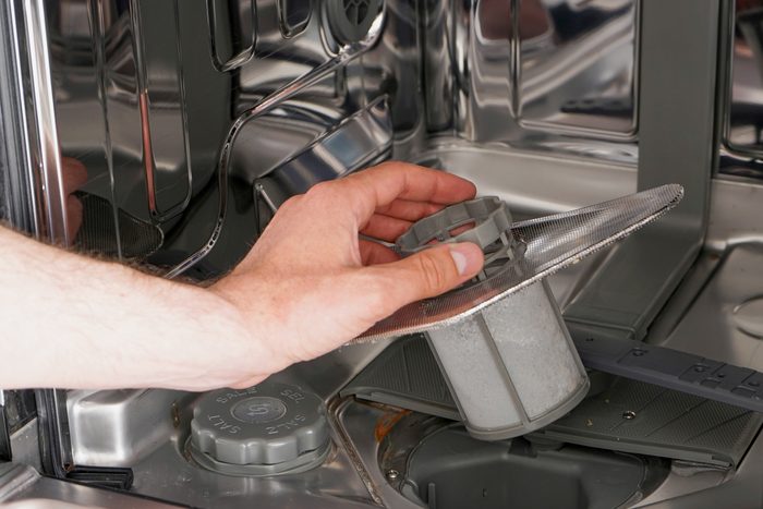 close up of a man's hand cleaning the filter in the dishwasher.