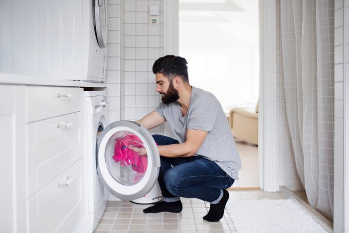 Side view of man crouching while loading clothes in washing machine at home