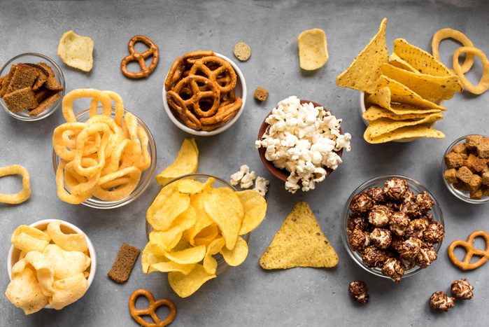 Assortment of Unhealthy Snacks: chips, popcorn, nachos, pretzels, onion rings in bowls