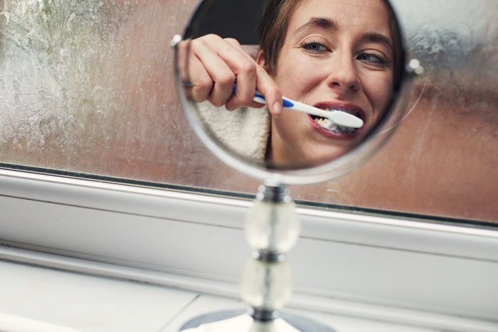 Woman looking in the mirror brushing her teeth