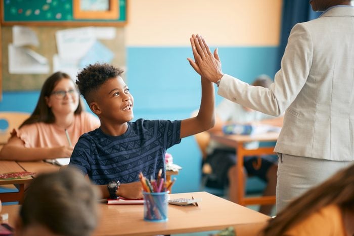 Happy black elementary student and his teacher giving high five during class at school.