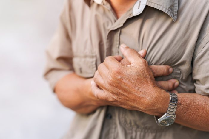 Close-up of an elderly man's hand held his chest in pain. Concept of heart disease.