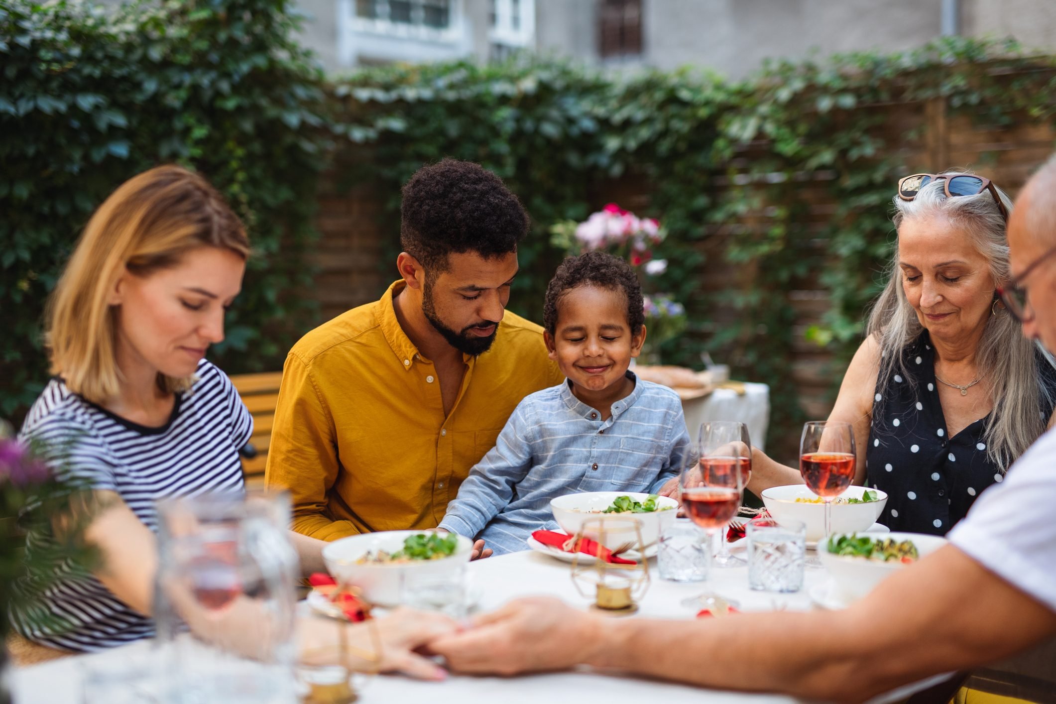 Portrait of multiracial three generations family praying together when dining outdoors in front or back yard.
