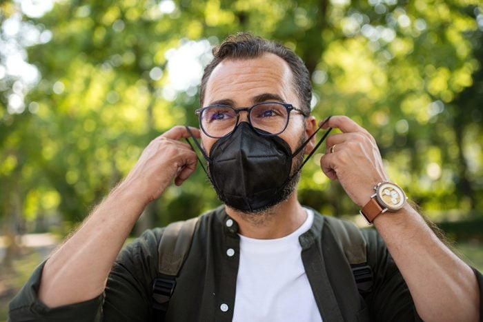 Portrait of mature man walking and putting on face mask outdoors in park.