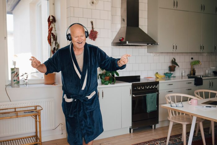 Cheerful senior man wearing headphones dancing in kitchen at home