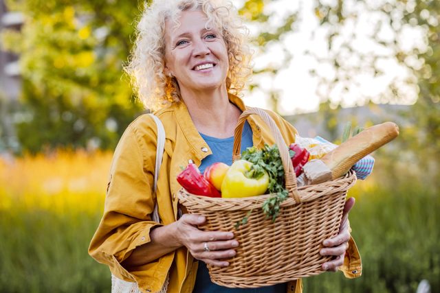 woman in casual clothes carrying fresh fruits and vegetables in a wicker basket