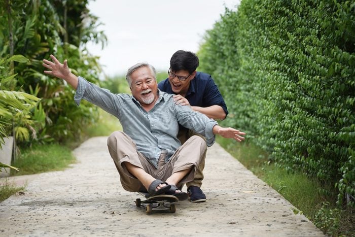 happy asian father sitting on a skateboard with his son behind him