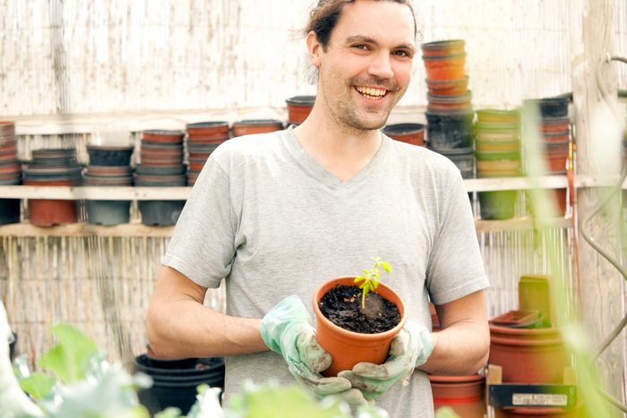 Smiling man holding flowerpot with Moringa seedling