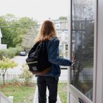 Teenage girl walking out the front door of her house. Back view of her leaving the house. She is on her way to school, wearing a back pack and holding the door open.
