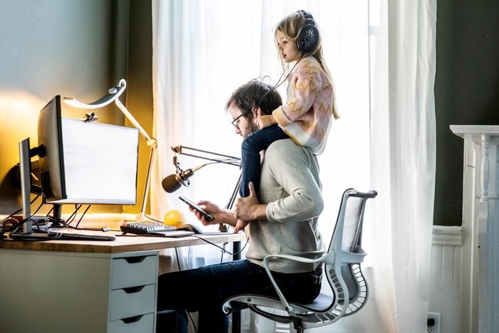 Father working in home office with young daughter on shoulders