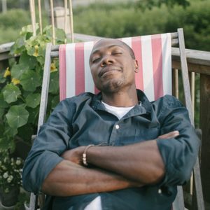 Mid adult man with closed eyes taking a nap on deck chair at porch