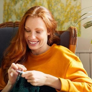 Woman knitting while sitting by plant on chair