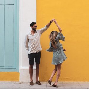 Full Length Of Couple Dancing On Sidewalk Against Yellow Wall