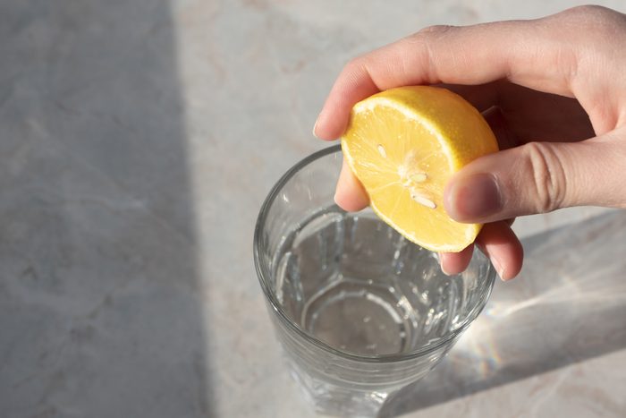 Women hand squeezes lemon juice in glass with soda water on marble table background