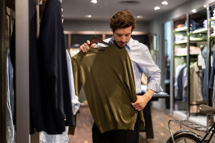 Latin american guy trying out a sweater on top at a men's clothing store