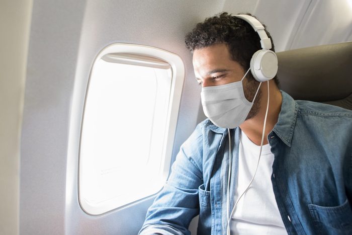 Man listening to music while flying on an airplane wearing a facemask
