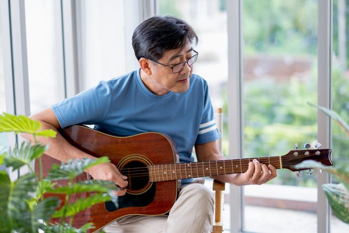 Asian old man as freelance artist sit in room and play guitar with relax emotion.