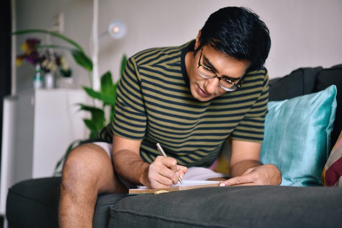 Man writing in a gratitude journal sitting on a sofa