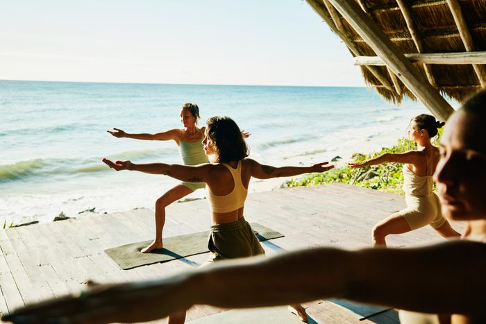 Wide shot of women in warrior pose while practicing yoga during class in ocean front pavilion at tropical resort