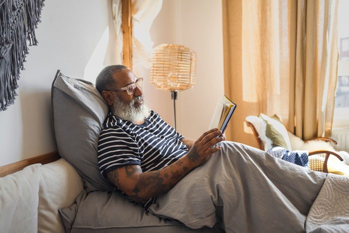 Senior man reading book while relaxing on bed at home