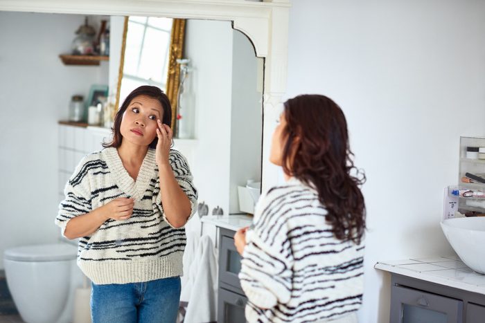 Mid adult woman applying eye cream and looking in mirror