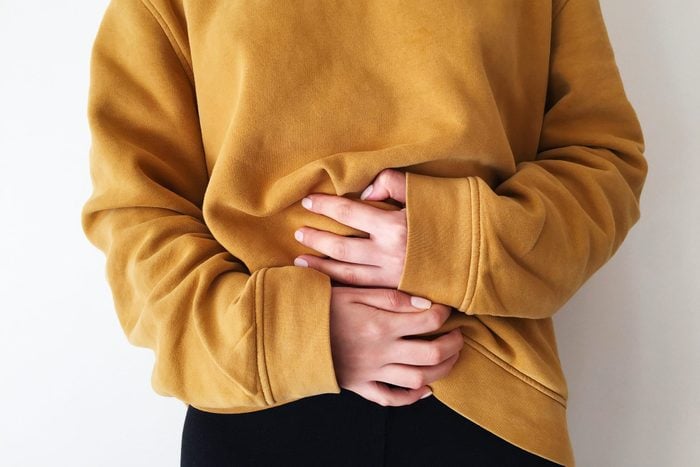 woman in a yellow sweatshirt holding her stomach