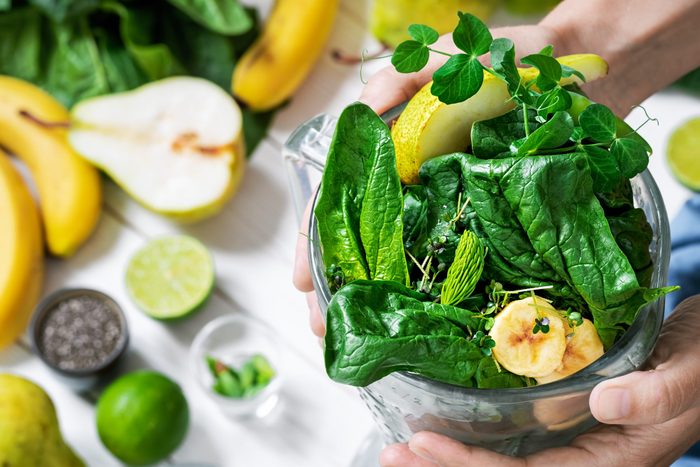 Woman is preparing a healthy detox drink in a blender - a smoothie with fresh fruits, green spinach and superfood seeds. Healthy lifestyle concept, ingredients for smoothies on the table, top view