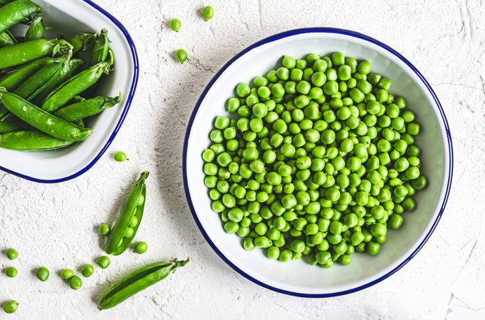 Green peas in a bowl with a bowl of pea shells to the side