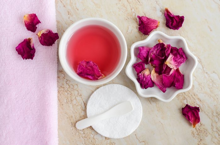 Two small white bowl with rose water (toner), dry rose petals and cotton pad. Ingredients for preparing homemade cosmetics. Natural beauty treatment recipe, zero waste concept. Top view, copy space