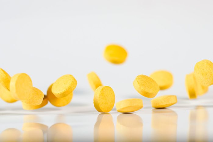 vitamin B2 yellow pills flying in mid air in white background