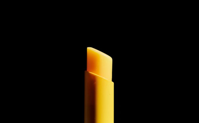 Close-up photo of a yellow lipstick, only upper half on a dark background