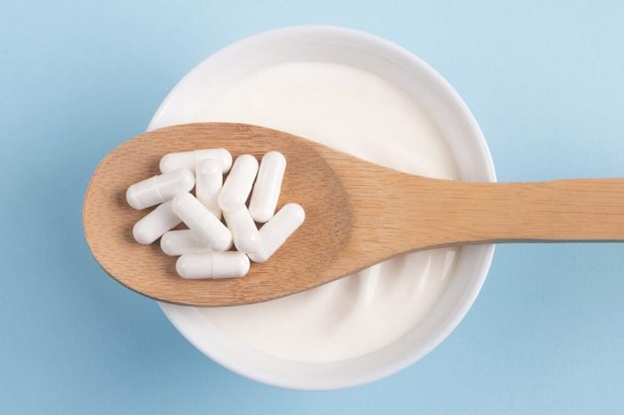 bowl of yogurt with a wooden spoonful of probiotic supplements resting on top, top view on a blue background