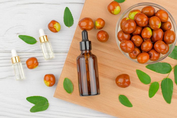 Jojoba oil in a bottle with a dropper and fresh jojoba fruits on a wooden table