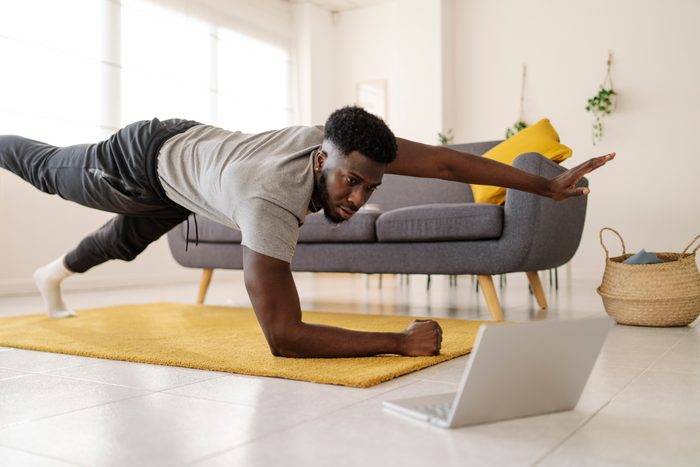 Man watching online exercise video on laptop while working out in the living room at home.