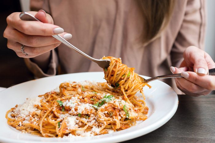 girl eats Italian pasta with tomato, meat. Close-up spaghetti Bolognese wind it around a fork with a spoon. Parmesan cheese