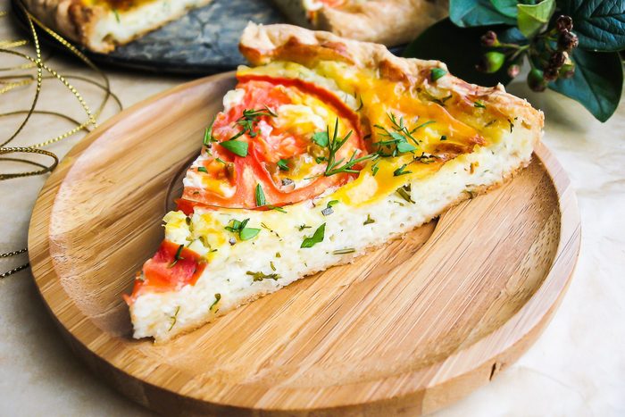 Slice of homemade tomato pie, pizza or quiche with curd cheese, eggs and fresh chopped parsley on a wooden plate perfect for summer picnic or snack, selective focus