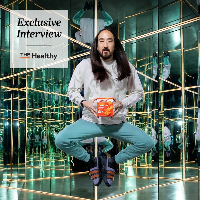 Steve Aoki floating holding a box of quest crackers with the healthy exclusive interview template