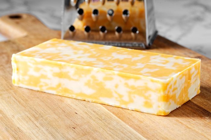 Block of colby jack cheese on a cutting board with a grater