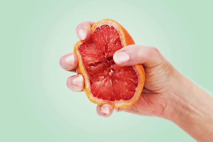hand squeezing a grapefruit on a green background