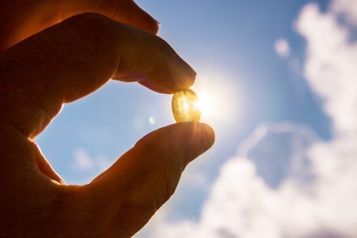 Vitamin D supplement being held with the sun in the background
