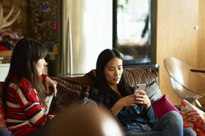 Chinese woman sitting on sofa with friend using cell phone