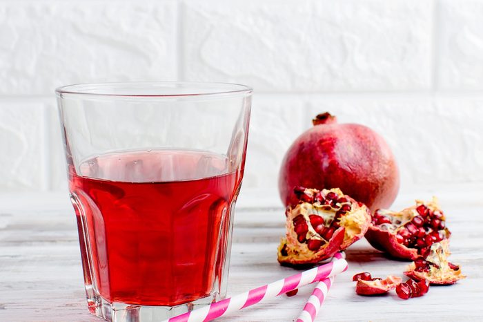 Close-Up Of Juice By Pomegranates In Glass Against Wall On Table