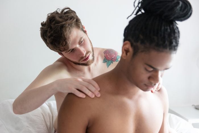 Young man massaging his male partner while both sitting on bed